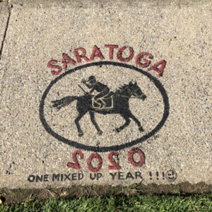 A humorous summer sidewalk drawing on Caroline Street in Saratoga Springs by C.A.M. Cameron shows a jockey riding backwards on a horse in a take on the standard silhouette of horse and rider. The numerals in the years are backwards, and underneath it says "2020: One mixed-up year!"